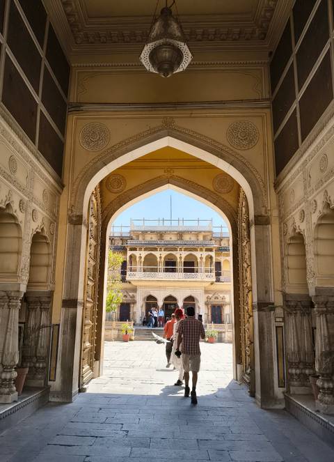       View through ornate archway to an inner palace courtyard where tourists gather.
  