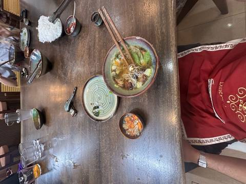       Bowl of Vietnamese noodle soup on rustic wooden table with chopsticks and dipping sauce.
  