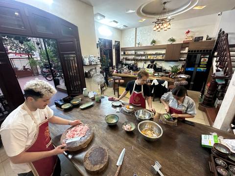       Participants wearing aprons preparing ingredients in a Vietnamese cooking class kitchen.
  
