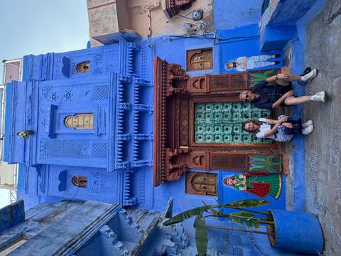       Couple seated in front of a vivid blue townhouse with ornate green door and folk murals in the Blue City.
  