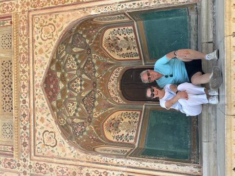       Couple poses beneath an ornate arched gateway inlayed with colorful floral motifs at Amber Fort.
  