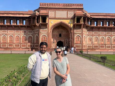       Visitor and local guide smile in front of the grand arched gateway of Agra Fort.
  