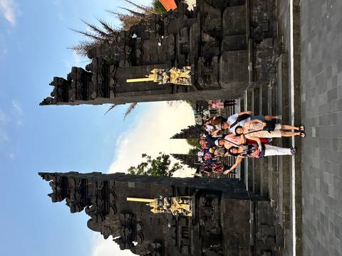       Group posing on stone steps between towering split gates at a Balinese temple.
  