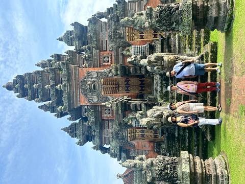       Travellers posing before a red-brick Balinese temple with intricate stone carvings.
  