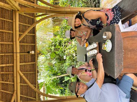       Small group enjoying a tea tasting session under a bamboo pavilion surrounded by lush garden.
  