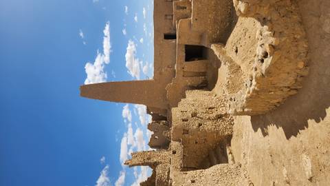       Ancient sand-colored ruins with a tall tapered tower rise against a bright blue desert sky.
  