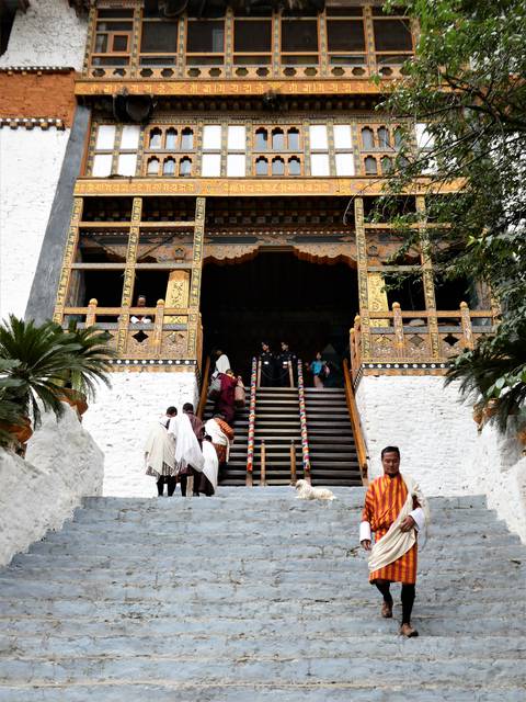       Visitors ascending the ornate staircase of a Bhutanese dzong with carved wooden balconies.
  