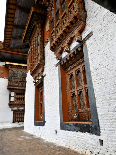       Close-up of ornate carved wooden windows and doorframes on a Bhutanese dzong.
  