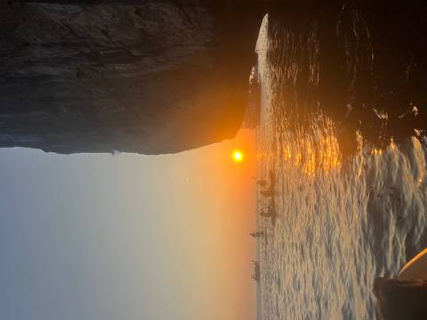       Silhouettes of kayakers paddling at sunset beneath a towering limestone cliff.
  