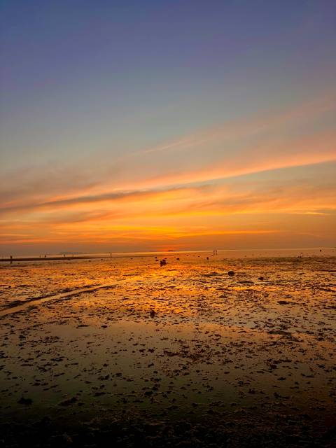       Wide tidal flat glowing orange and pink beneath a dramatic sunset sky.
  