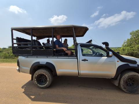       Open-sided safari jeep carrying tourists along a dusty road with green bushland behind
  