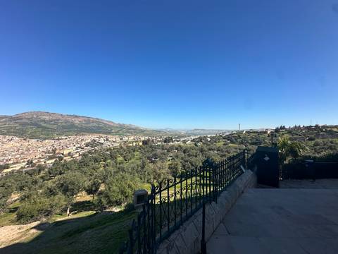       Wide valley view over Fes from a hilltop lookout with wrought-iron fence in the foreground.
  