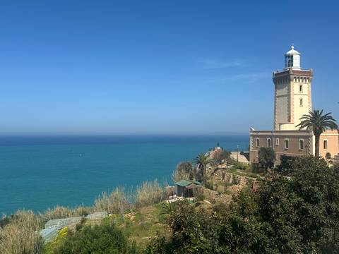      Cap Spartel lighthouse overlooking the vivid blue Atlantic Ocean and coastal gardens near Tangier.
  