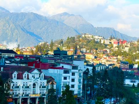       Colorful mountainous townscape in Sapa with peaks looming behind clusters of buildings.
  