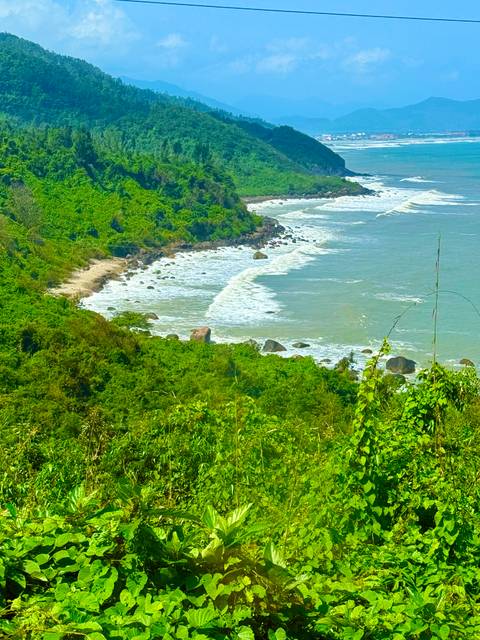       Remote coastline with waves crashing onto a green, forested headland in central Vietnam.
  