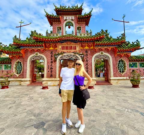       Couple stands in front of the ornate pink Fujian Assembly Hall gate in Hoi An.
  
