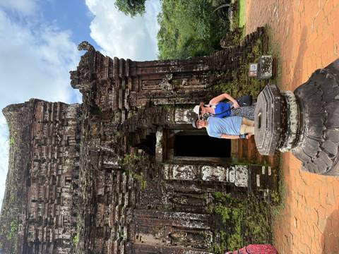       Two travellers pose before the weathered Hindu temple ruins of My Son Sanctuary.
  