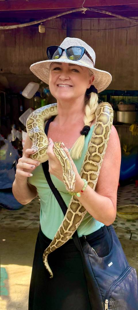       Woman holds a python draped over her shoulders during a wildlife encounter in the Mekong Delta.
  