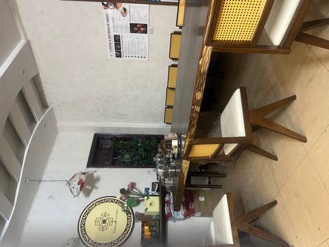       Simple dining room with wooden tables, rattan chairs and coffee equipment against a white wall.
  