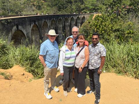       Group of travellers stand before the iconic Nine Arch Bridge amid lush greenery.
  