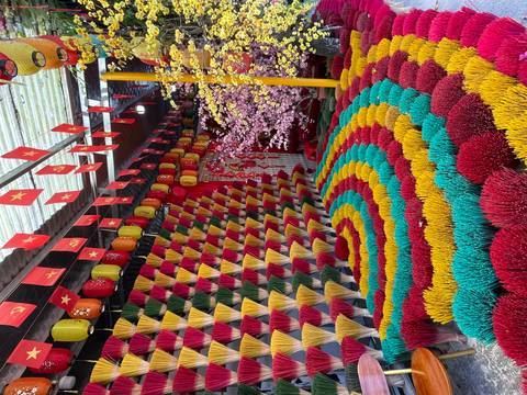       Vibrant spirals of multicolored incense sticks displayed with Vietnamese flags overhead.
  