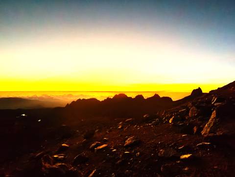       Silhouetted jagged peaks of Mount Kenya against a vivid yellow dawn horizon.
  