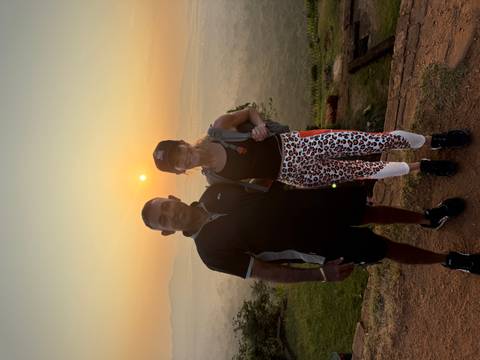       Guide and traveler smiling at sunrise on a scenic hilltop with misty plains below in Sri Lanka.
  