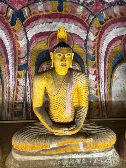       Golden Buddha statue illuminated inside a richly painted chamber at Dambulla Cave Temple.
  