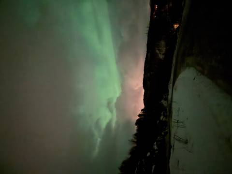      Green aurora borealis sweeping across a cloudy night sky above snowy terrain.
  