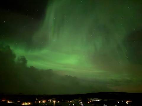       Faint curtains of green aurora glow in a cloud-streaked Arctic night sky.
  