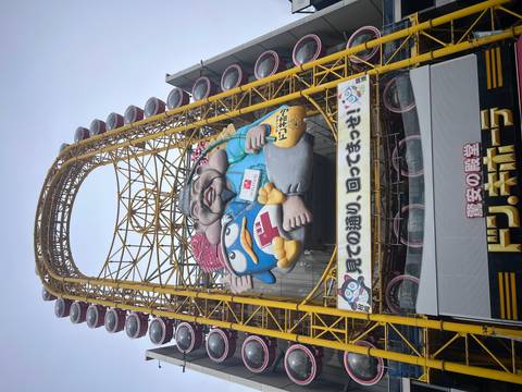       Tall yellow Ferris wheel with a cartoon mascot dominates the facade of a Don Quijote store.
  