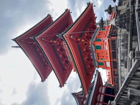       Striking vermillion three-tiered pagoda of Kiyomizu-dera temple stands against a moody sky.
  