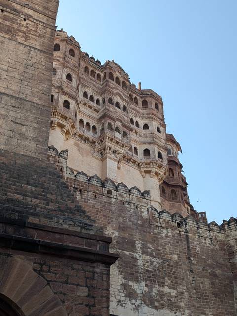       Stone bastions and intricate balconies of Mehrangarh Fort rise dramatically into a clear sky.
  