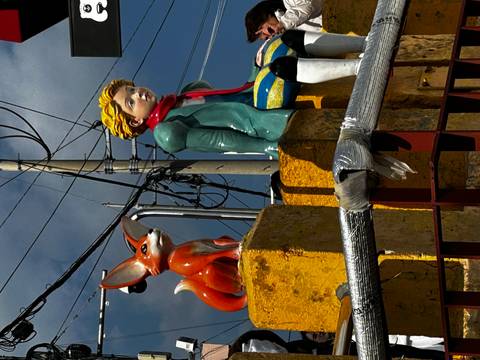       Statues of the Little Prince and fox sit atop colourful wall beneath power lines and blue sky.
  