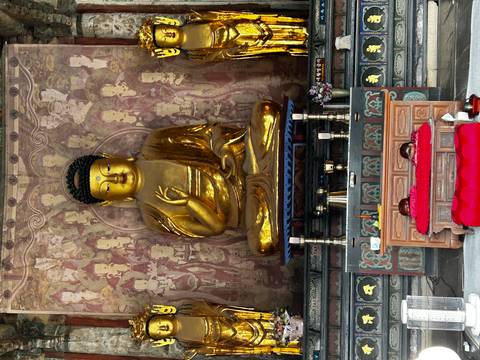       Large golden seated Buddha statue inside richly decorated temple shrine.
  