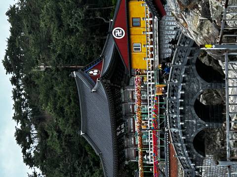       Traditional seaside temple with arching stone bridge, colourful lanterns and pine-covered hill backdrop.
  