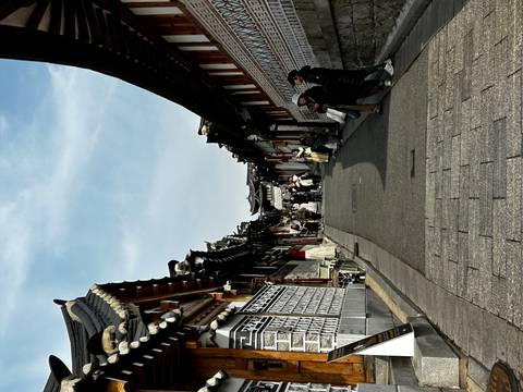       Traditional Korean alley of hanok houses bustling with visitors dressed in hanbok.
  