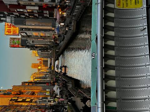       Evening light reflects on canal lined with neon-lit buildings and bridges in Osaka.
  