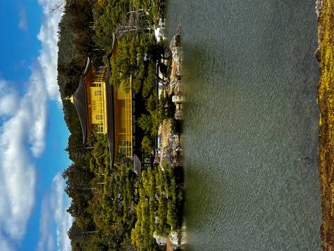       Golden Kinkaku-ji pavilion reflected in serene pond surrounded by green pines under blue sky.
  