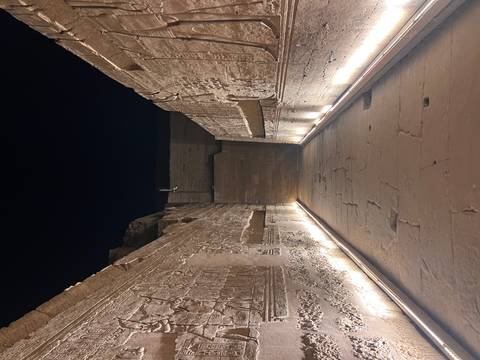       Narrow temple corridor illuminated from below, revealing detailed hieroglyphic reliefs on both walls.
  