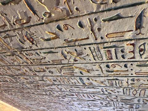       Close-up of vividly colored hieroglyphs carved into a temple wall, showcasing birds, eyes and symbols.
  