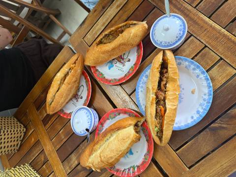       Four Vietnamese banh mi sandwiches served on floral plates atop a wooden table.
  