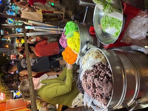       Vendor serves brightly coloured sticky rice at a busy Vietnamese night market stall.
  
