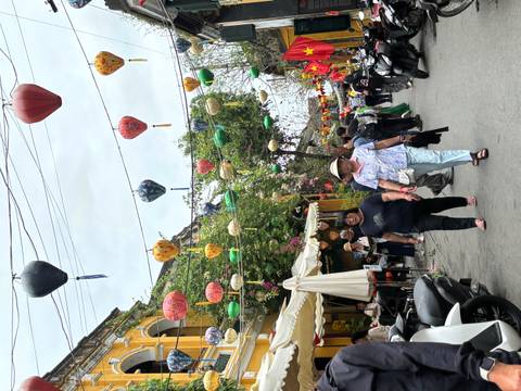       Lantern-festooned street in Hoi An Old Town with locals and tourists walking beneath colourful lamps.
  