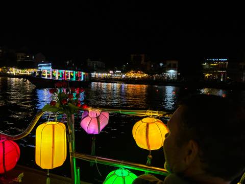       Colourful lanterns glow on a small boat as it drifts along a river at night.
  