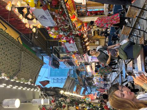       Busy Hanoi Train Street lined with cafes, lights and people walking beside the tracks.
  