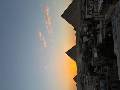      Silhouetted pyramids of Giza against an orange sunset sky above the outskirts of Cairo.
  