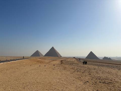       Wide desert vista with the Pyramids of Giza and small figures of tourists walking across the sand.
  