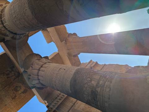       Sunlight streams past the carved stone columns of Kom Ombo Temple creating lens flare.
  