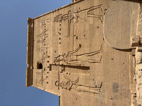       Stone wall with large carved figures and hieroglyphs at Edfu Temple.
  